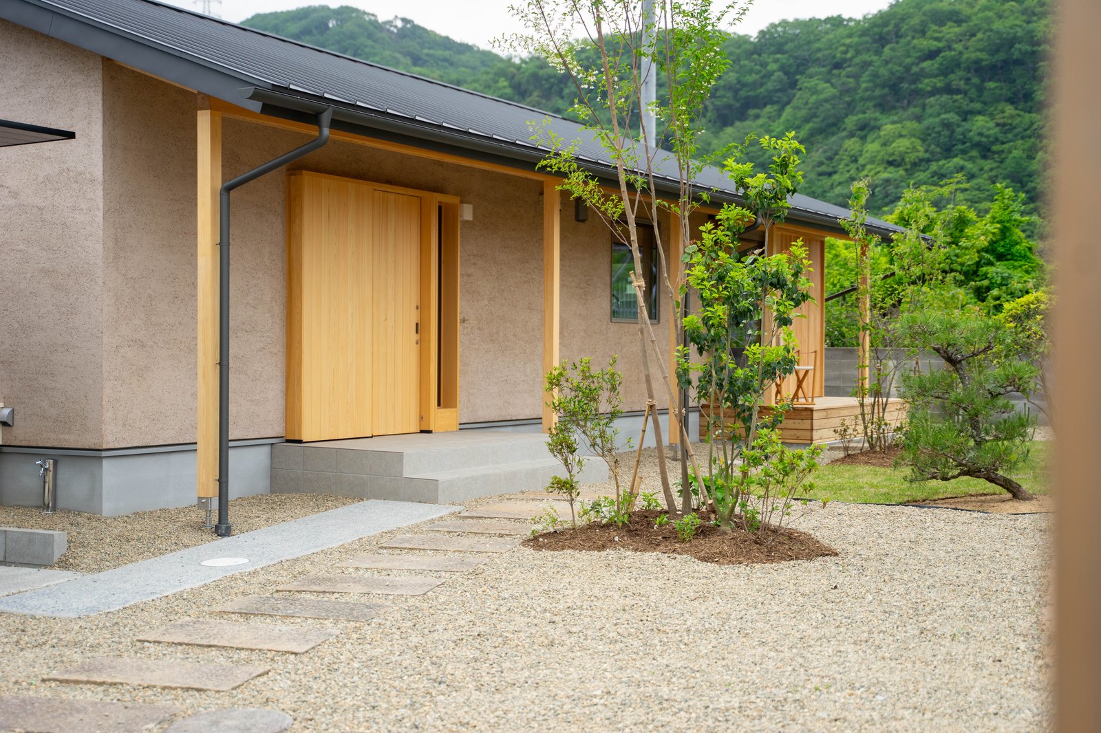 木製玄関ドアと軒の深いアプローチのある平屋